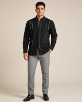 Man wearing a black leopard guayabera shirt with gray pants on a beige background