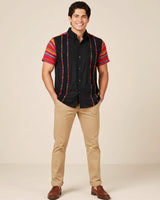 Man wearing a black guayabera shirt with zarape sleeves against a beige background