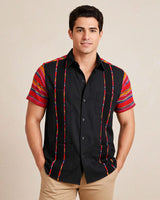 Man wearing a black guayabera shirt with zarape sleeves against a beige background