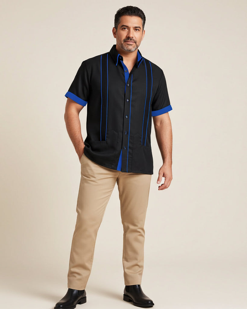 Man wearing a black guayabera shirt with blue accents and beige pants on a beige background