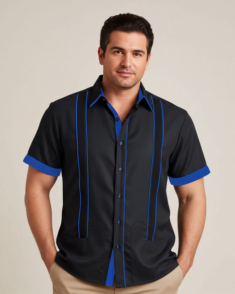 Man wearing a black guayabera shirt with blue accents and beige pants on a beige background