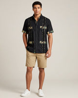 Man wearing a black camo guayabera shirt and beige shorts on a plain background