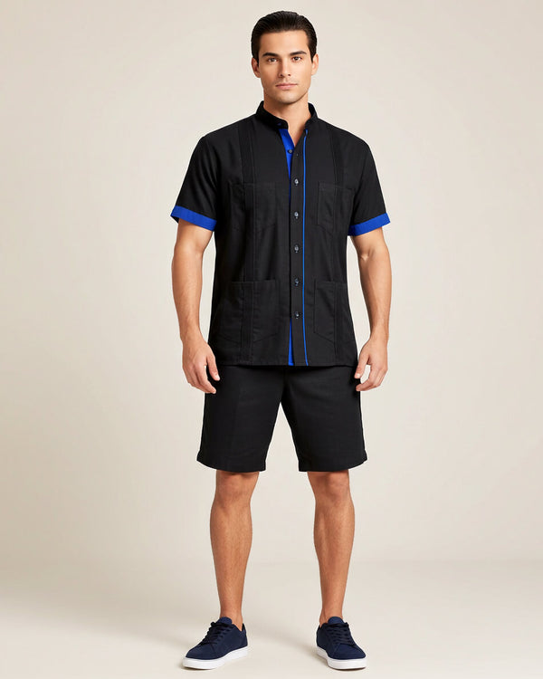 Man wearing a black guayabera shirt with blue accents and black shorts on a beige background
