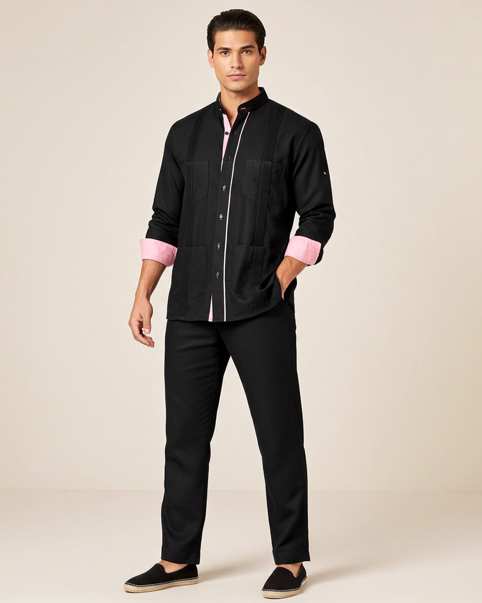 Man wearing a black guayabera shirt with pink cuffs and black pants on a beige background