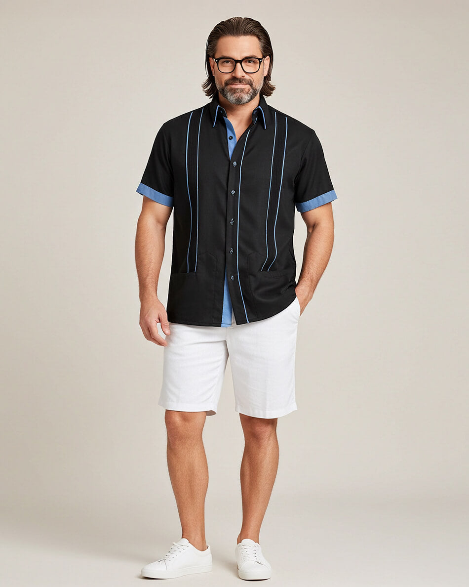 Man wearing a black guayabera short-sleeve shirt with blue accents and white shorts on a beige background