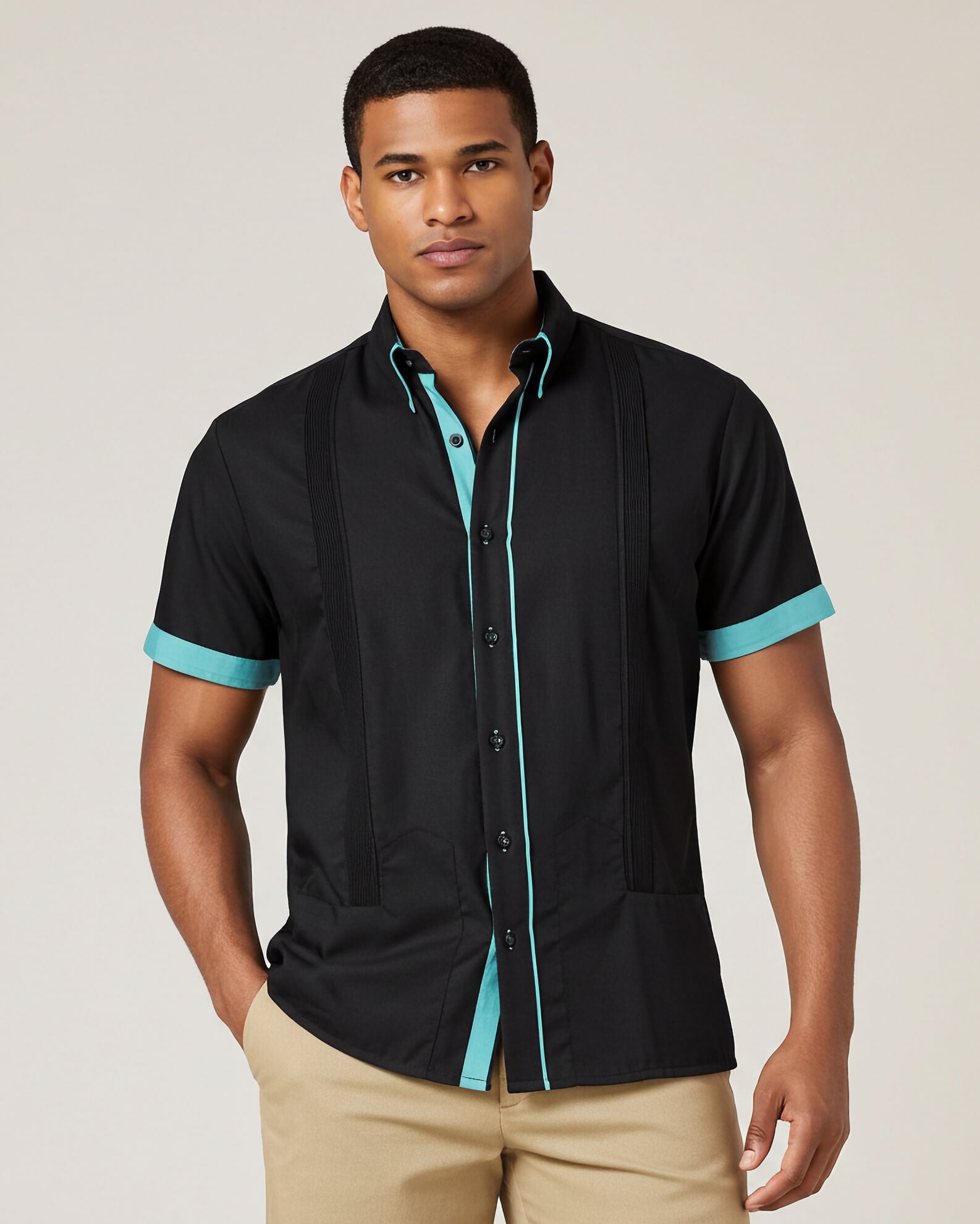 Man wearing a black guayabera shirt with turquoise trim on a plain background