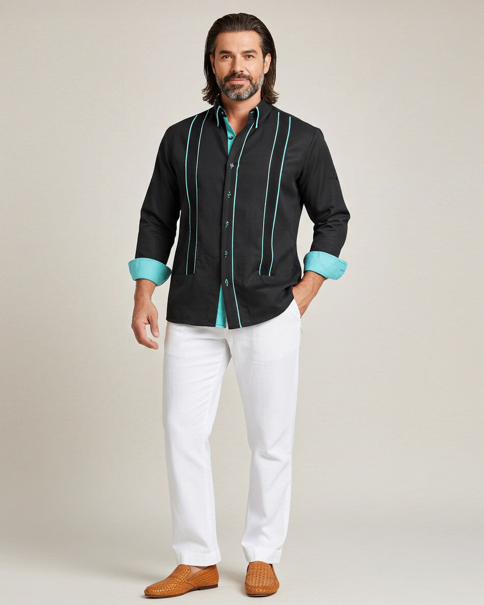 Man wearing a black guayabera shirt with teal accents and white pants on a plain background