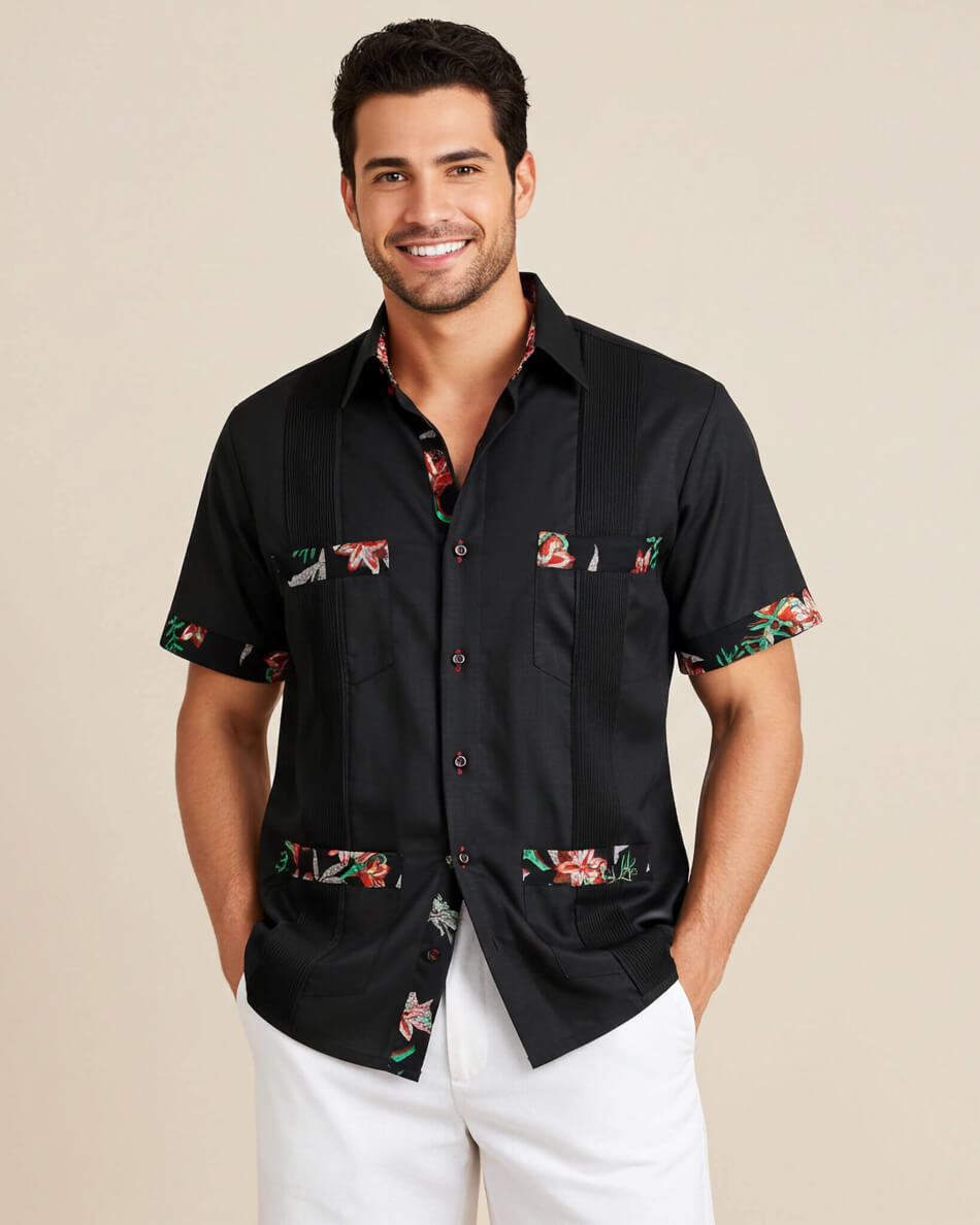 Man wearing a black guayabera shirt with colorful floral patterns on a beige background