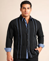 Man wearing a black guayabera shirt with blue gingham accents and cuffs on a beige background