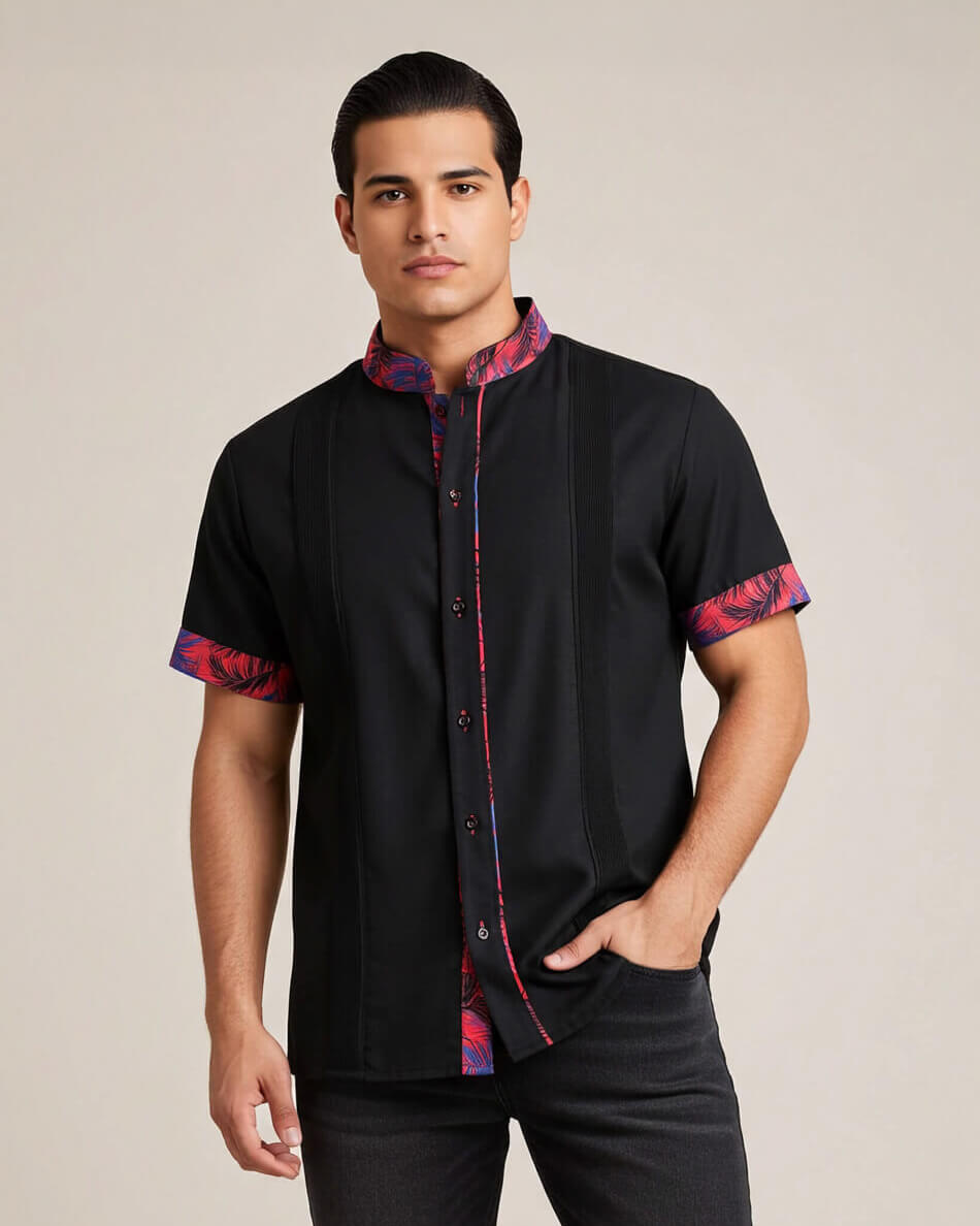 Man wearing a black guayabera shirt with colorful patterns on sleeves and collar against a beige background