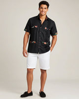 Man wearing a black guayabera shirt and white shorts on a plain background