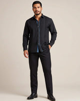 Man wearing a black long sleeve guayabera shirt with turquoise gingham accents on a beige background