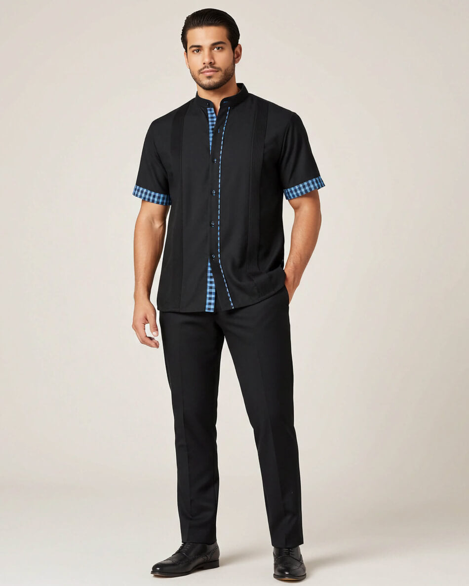 Man wearing a black short sleeve guayabera shirt with turquoise gingham accents on a beige background