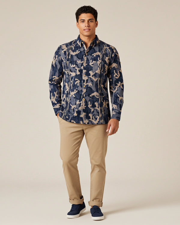Man wearing a navy patterned camo guayabera shirt and beige pants on a beige background