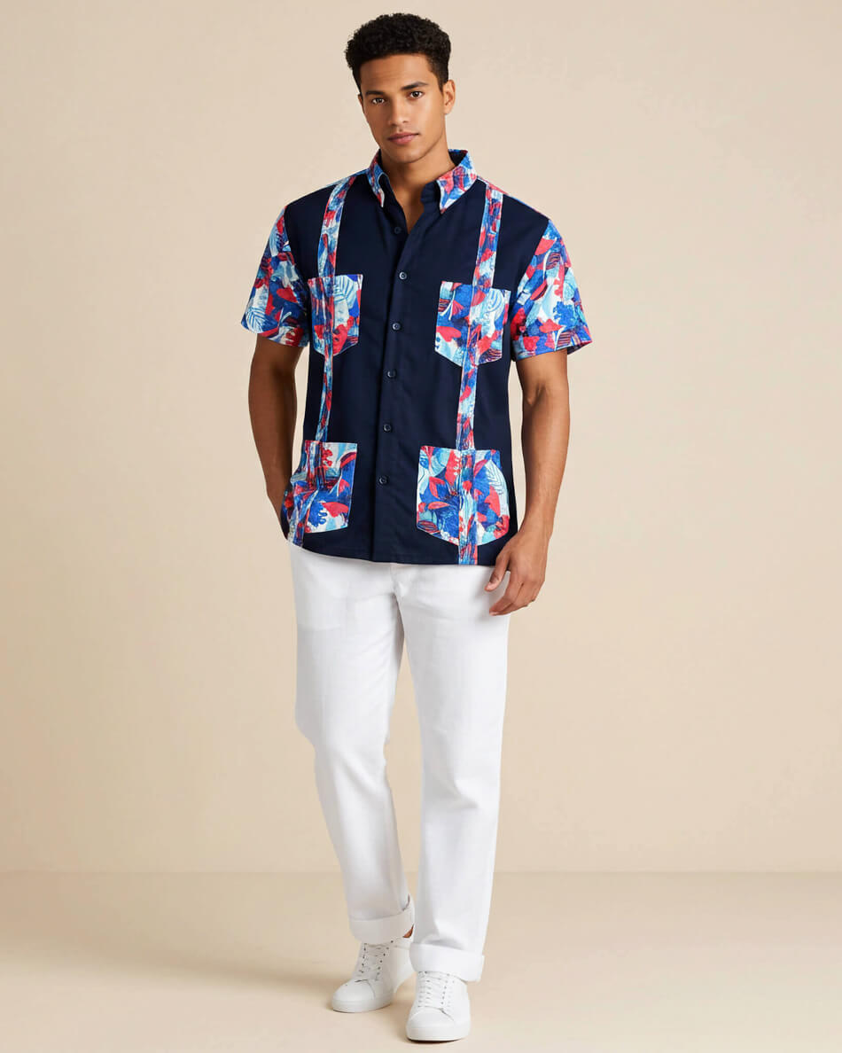 Man wearing a navy guayabera shirt with colorful floral patterns and white pants on a beige background