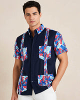 Man wearing a navy guayabera shirt with colorful floral patterns on a beige background