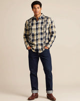 Man wearing a plaid shirt and dark jeans against a beige background
