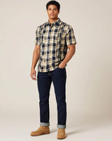 Man wearing a plaid shirt, denims, and brown boots on a plain background