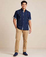 Man wearing a navy guayabera shirt and beige pants on a beige background