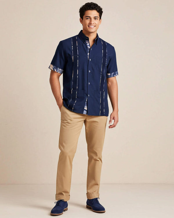 Man wearing a navy guayabera shirt and beige pants on a beige background