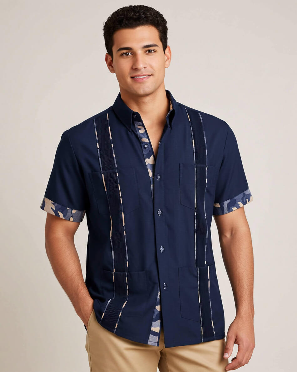 Man wearing a navy blue guayabera shirt with camo accents with beige pants on a plain background