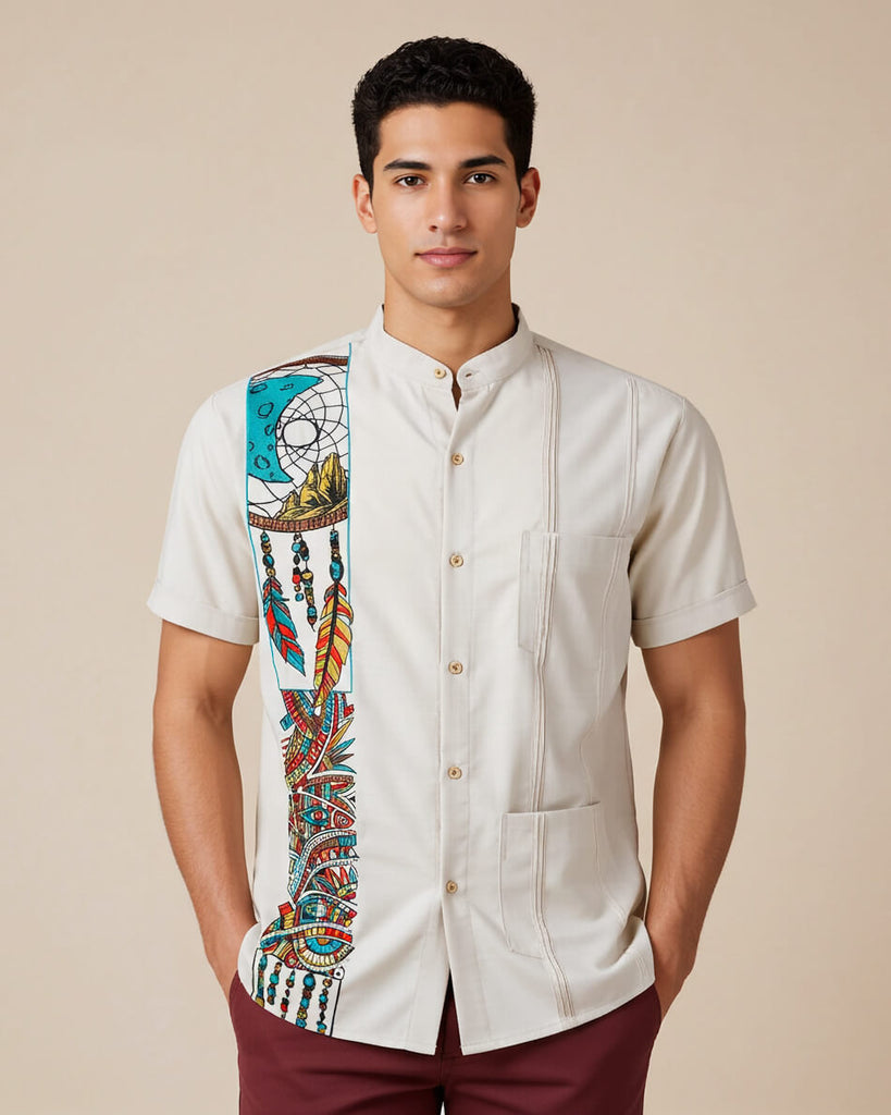 Man wearing a beige guayabera shirt with detailed dreamcatcher embroidery and maroon pants on a beige background