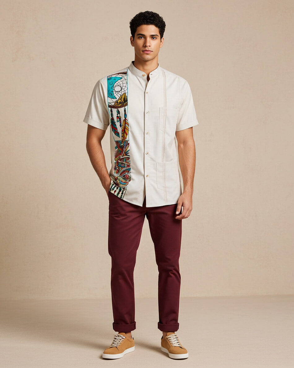 Man wearing a beige guayabera shirt with dreamcatcher and feather embroidery and maroon pants on a beige background