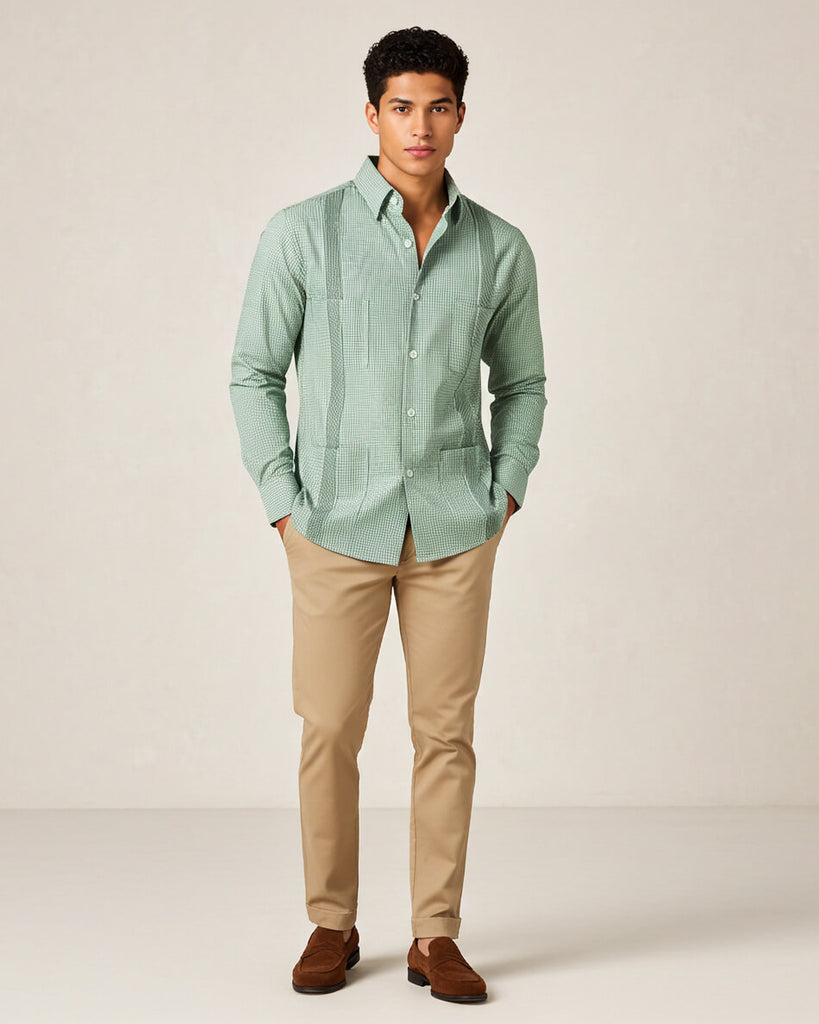 Man wearing a light green gingham patterned guayabera shirt with beige pants on a plain background