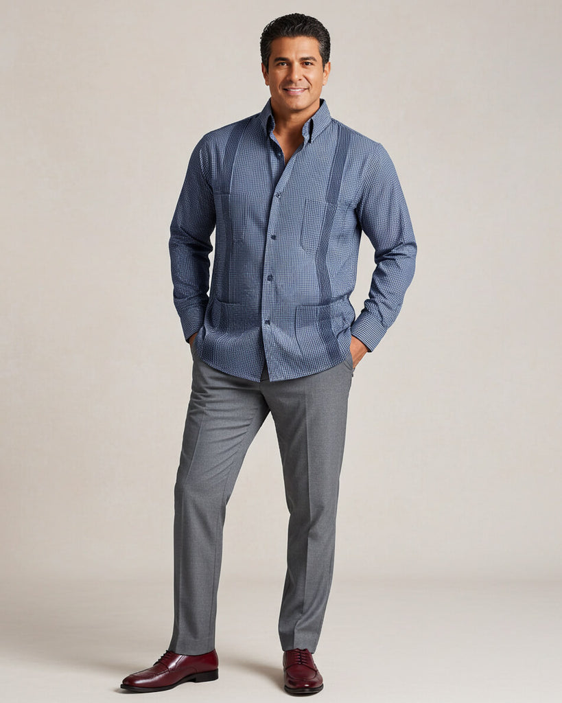 Man wearing a blue gingham patterned guayabera shirt and gray pants on a beige background