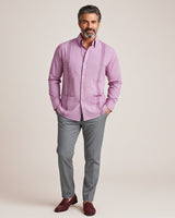 Man wearing a pink guayabera shirt and gray pants against a beige background