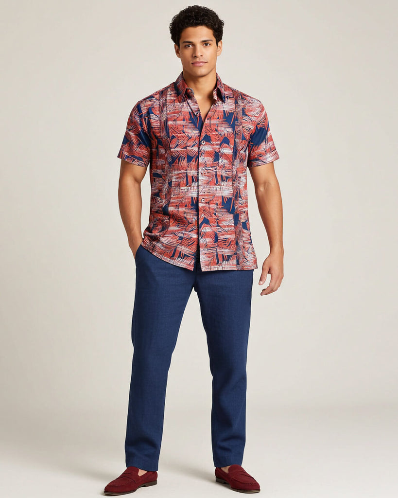 Man wearing a patterned guayabera shirt and blue pants on a plain background