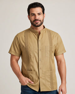 Man wearing a khaki guayabera short-sleeve shirt with pleat details on a plain background