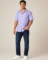 Man wearing a light purple guayabera shirt and dark blue jeans against a beige background