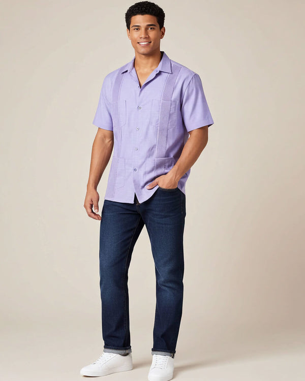 Man wearing a light purple guayabera shirt and dark blue jeans against a beige background