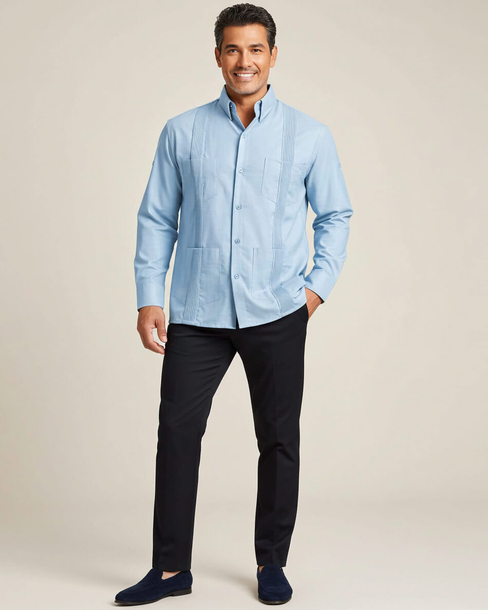 Man wearing a light blue guayabera shirt and black pants on a beige background