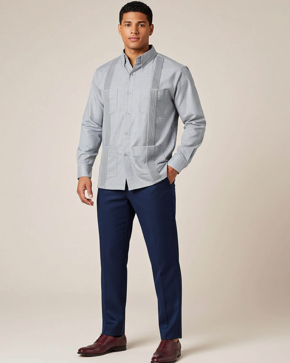 Man wearing a light grey guayabera shirt and dark blue pants against a beige background