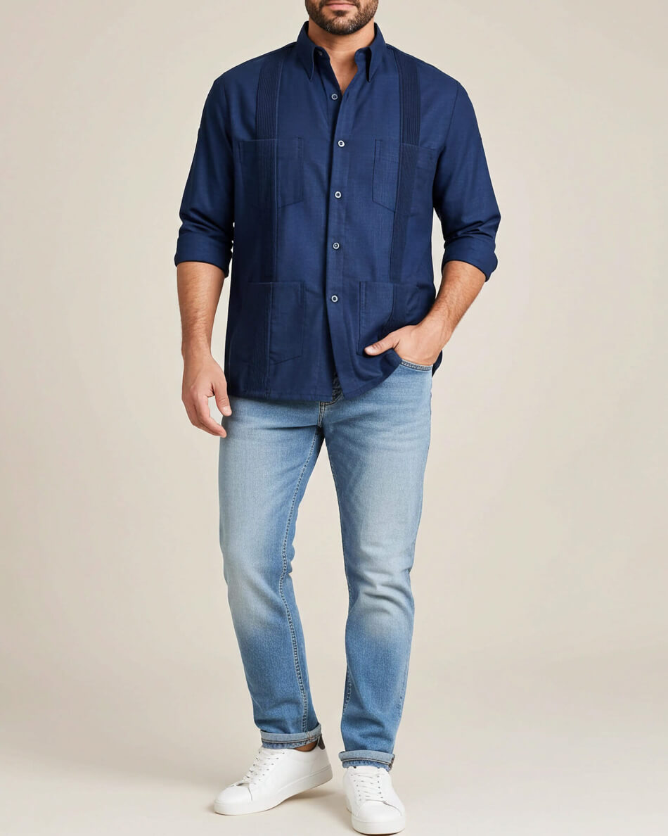 Man wearing a navy blue guayabera shirt and light blue jeans on a beige background