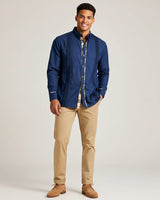 Man wearing a blue long-sleeve guayabera shirt and beige pants on a light background