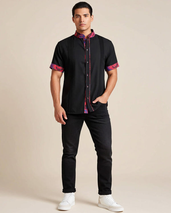 Man wearing a black guayabera shirt with colorful accents and black jeans on a beige background