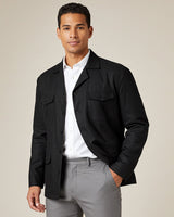 Man wearing a black guayabera jacket over a white shirt and gray pants on a beige background