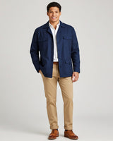 Man wearing a navy guayabera shirt jacket, white shirt, beige pants, and brown shoes on a light gray background