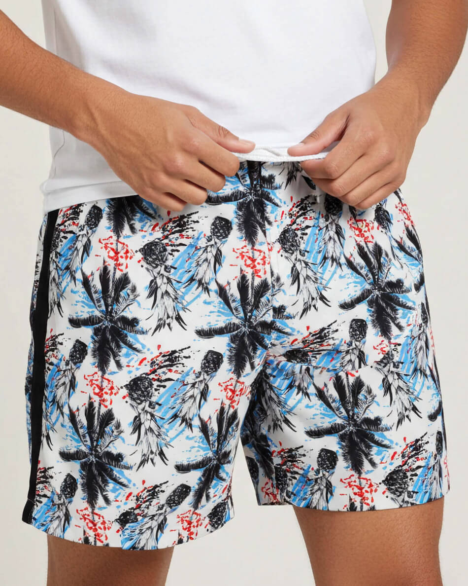 Person wearing a white shirt and floral shorts with black, blue, and red patterns on a light gray background