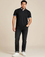 Man wearing a charcoal grey polo shirt with camo accents and black jeans on a beige background