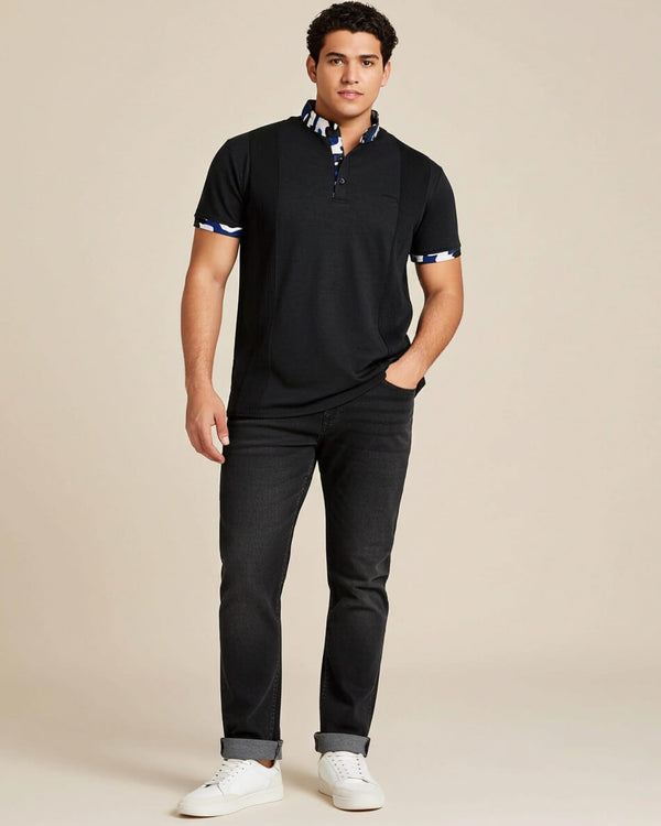 Man wearing a charcoal grey polo shirt with camo accents and black jeans on a beige background