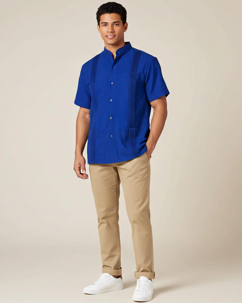Man wearing a blue guayabera linen shirt and beige pants on a plain background