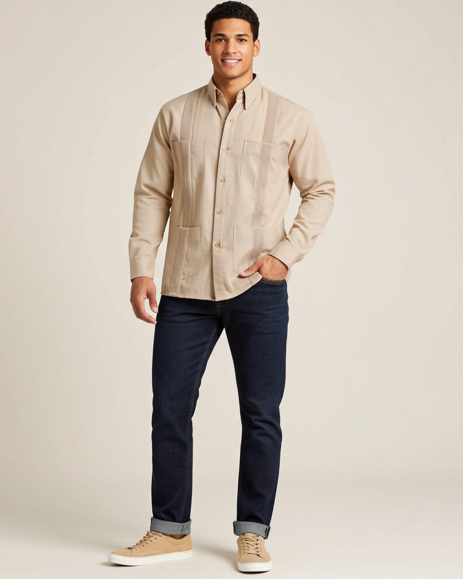 Man wearing a beige button-up guayabera shirt and dark jeans on a plain background