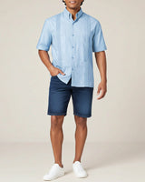 Man wearing a light blue short-sleeve guayabera shirt and dark blue shorts on a beige background