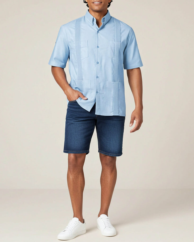 Man wearing a light blue short-sleeve guayabera shirt and dark blue shorts on a beige background