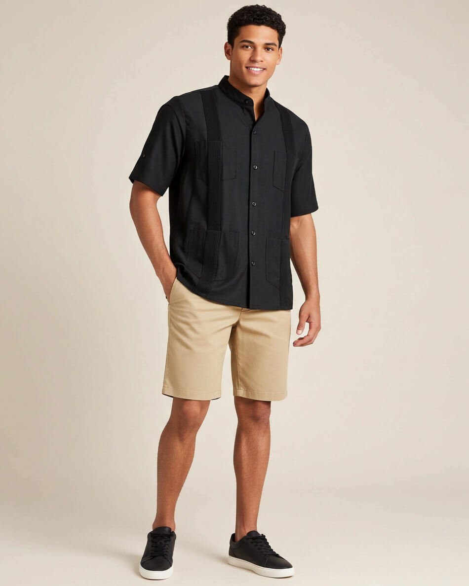 Man wearing a black short-sleeve guayabera shirt and beige shorts on a beige background