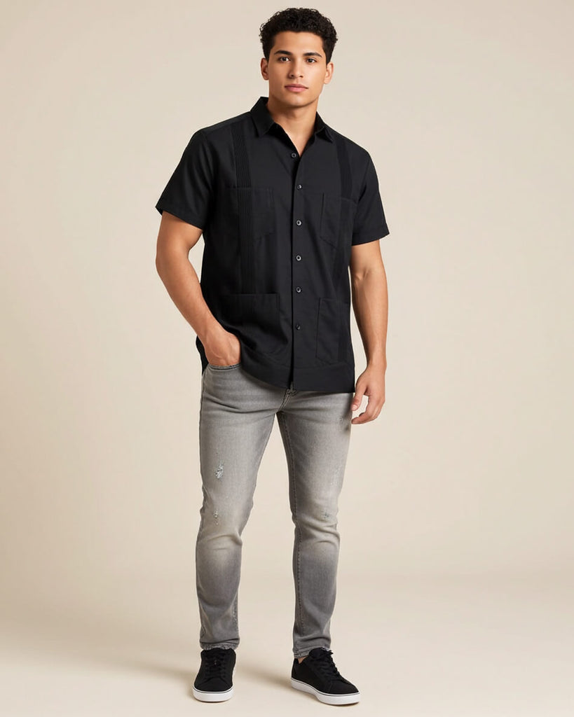 Man wearing a black short-sleeve button-up guayabera shirt and gray jeans on a beige background